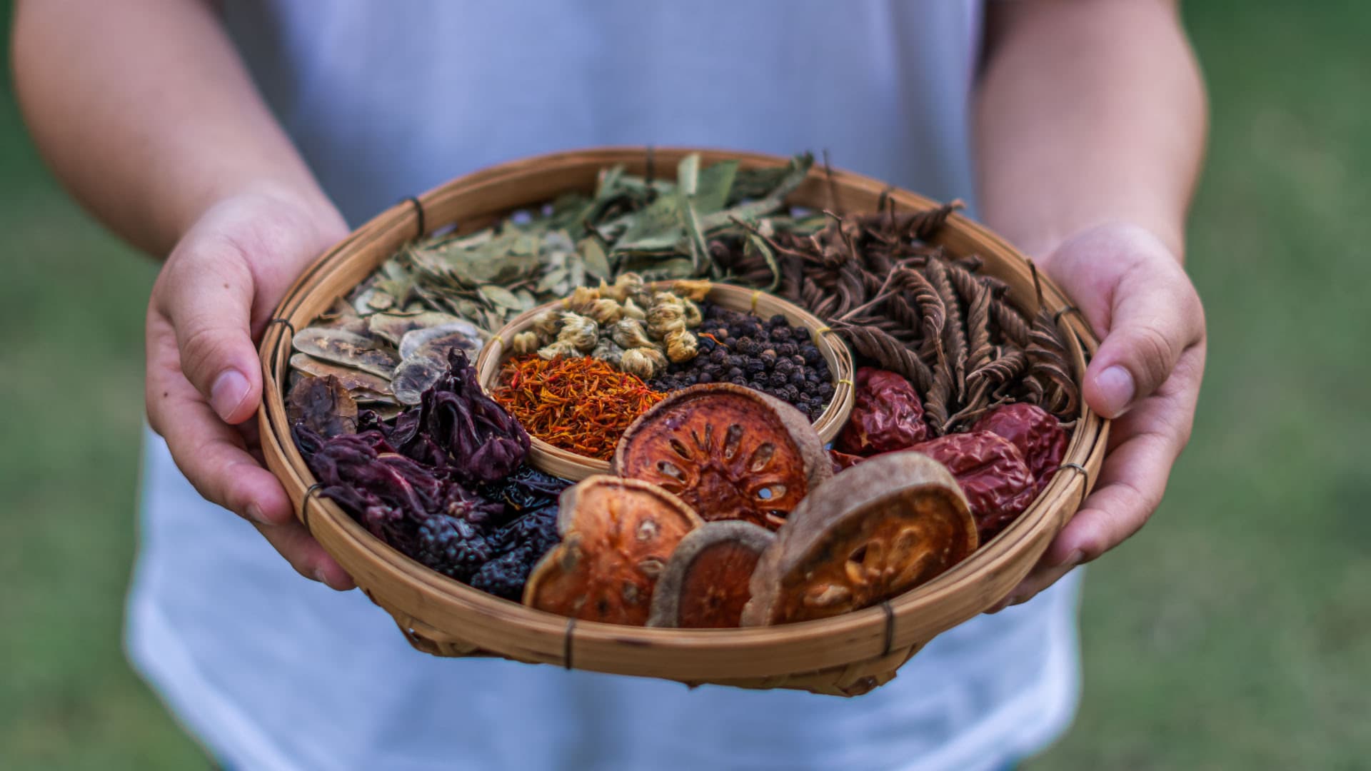 Hands holding a woven basket of dried flowers, spices and herbs